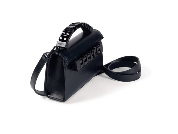 Side angle view of Mini Jewel Top Handle handbag with closer view of black tonal hardware. The top handle and front plaque hardware each have an etched Bentz name logo. The detachable shoulder strap matches the handbag’s smooth black leather.